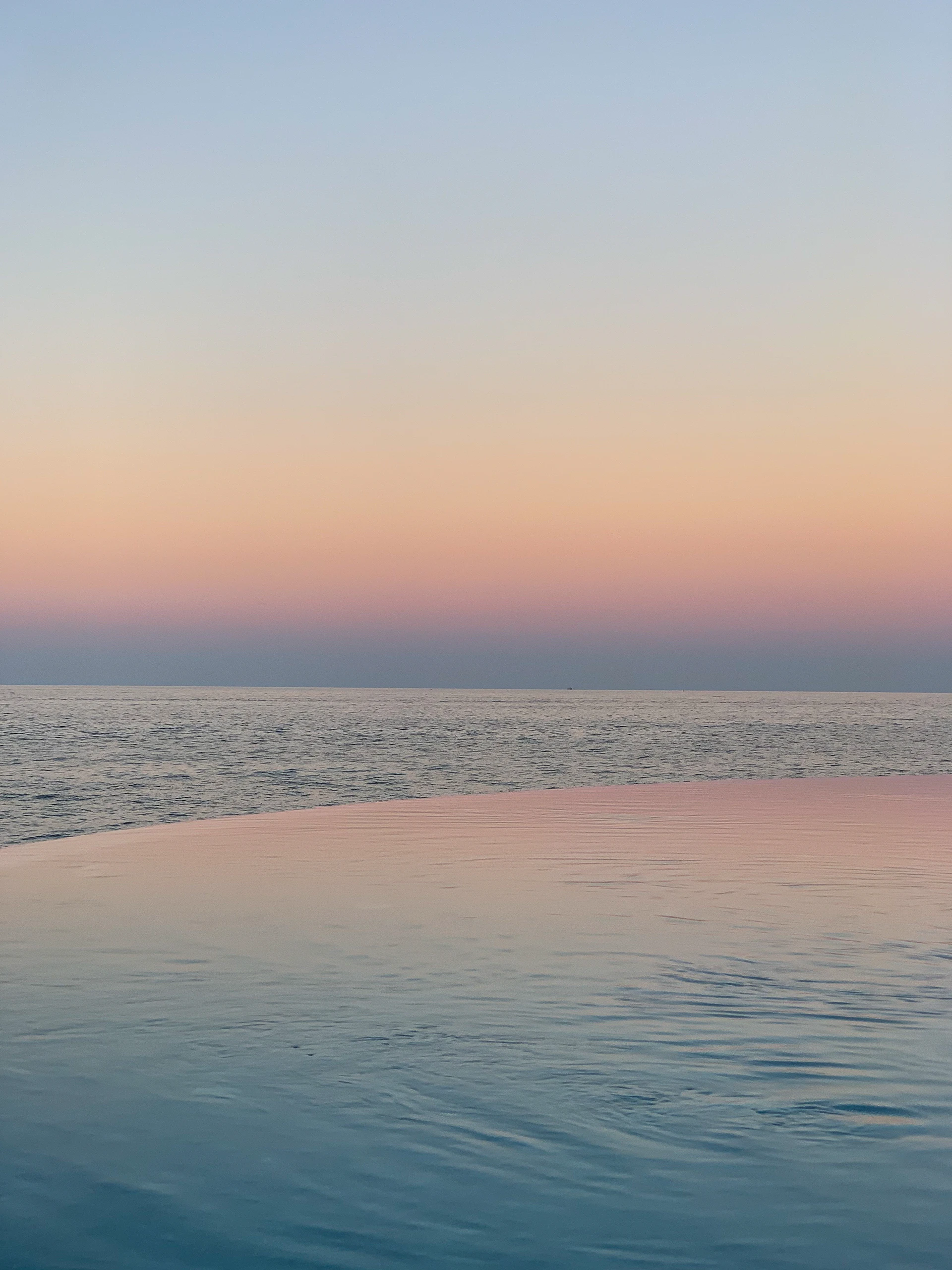 Infinity pool edge dissolving into the ocean horizon at sunset